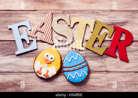 Un grand angle tourné de différentes lettres formant le mot Easter et deux biscuits décoré comme un oeuf de pâques décorés et qu'un drôle de chick on a rustic wo Banque D'Images