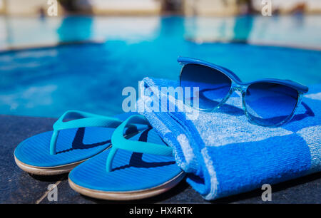 Chaussons bleu, lunettes de soleil et serviettes sur la bordure d'une piscine - maison de vacances concept tropical Banque D'Images