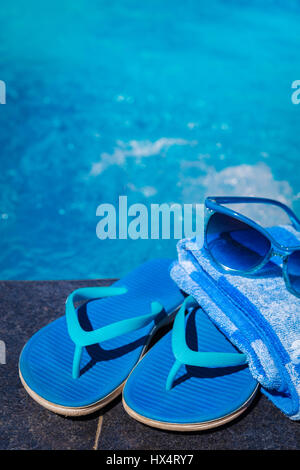 Chaussons bleu, lunettes de soleil et serviettes sur la bordure d'une piscine - maison de vacances concept tropical Banque D'Images