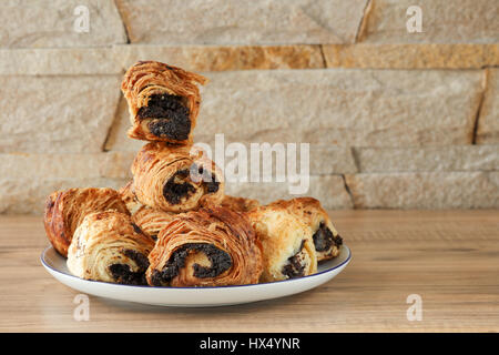 Brioches sucrées aux graines de pavot sur une assiette de porcelaine blanche avec une bordure bleue et sur une table en bois et contre un mur de pierre - grès. Banque D'Images