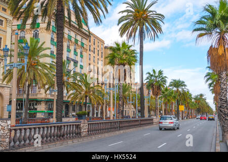 Voitures dans la rue, la fin de l'après-midi à Barcelone. Rue bordée de palmiers avec vacances & condo buildings aux gens de se rencontrer dans un café à l'autre côté de la rue. Banque D'Images