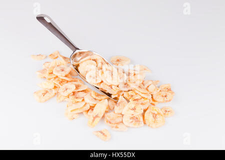 Metal écope dans un tas de tranches de bananes séchées sur une surface blanche. Bananes tranches isolé sur fond blanc. Banque D'Images