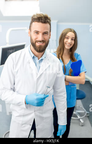 Portrait of handsome dentiste avec de jeunes femmes en uniforme à l'assistant de cabinet dentaire Banque D'Images