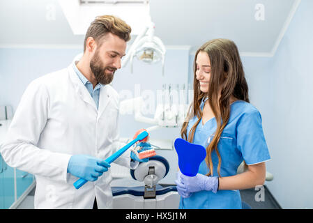 Beau dentiste montrant comment brosser les dents sur la mâchoire artificielle pour les jeunes femmes étudiant à l'dental office Banque D'Images