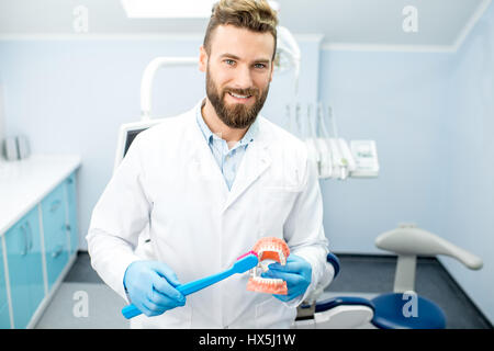 Portrait of handsome dentiste en uniforme avec grande brosse à dents et de la mâchoire artificielle au cabinet dentaire Banque D'Images