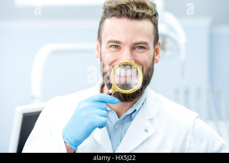 Portrait of handsome dentiste holding loupe devant son sourire à pleines dents le cabinet dentaire Banque D'Images