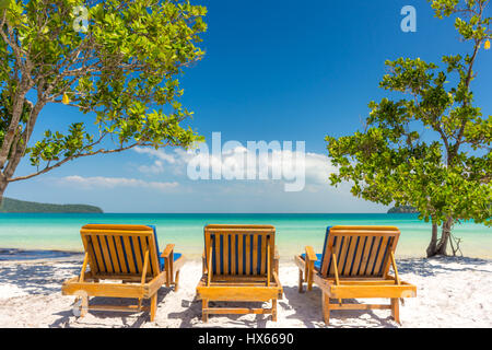 Three sun loungers on a white sand beach looking out to a tranquil empty tropical sea. Low angle. Banque D'Images