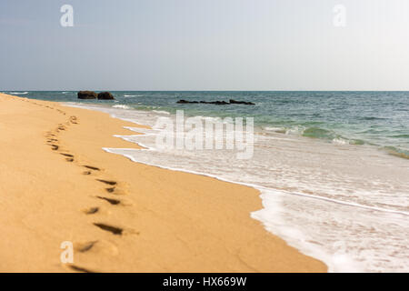 Une ligne de pied imprime dans une plage de sable doré avec de l'eau de mer à la plage. Banque D'Images