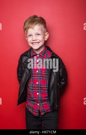 Fashion petit garçon portant une veste en cuir. Studio portrait sur fond rouge Banque D'Images