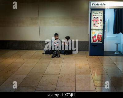 Deux personnes de manger le déjeuner sur le plancher à côté d'un photo-me istant Photo Booth dans un centre commercial de Cambridge Banque D'Images