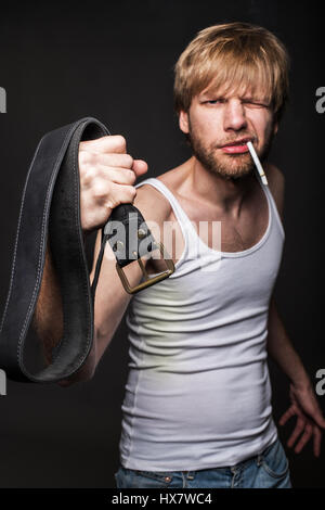 Homme en colère menace avec ceinture. Concept : La violence contre les femmes. Studio portrait sur fond noir Banque D'Images