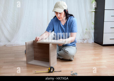 Une femme de race blanche d'auto assemblage de nouveaux meubles assis sur le plancher. Banque D'Images