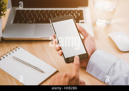 Businessman hand holding un téléphone avec écran isolé au-dessus du bureau de l'office Banque D'Images