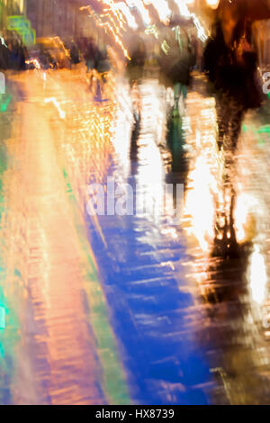 Résumé fond de personnes chiffres sous les parapluies, ville dans la pluie. Réflexions lumineuses des lampes dans des trottoirs mouillés. Flou de mouvement intentionnel. Concept de modernisation de la ville. Banque D'Images