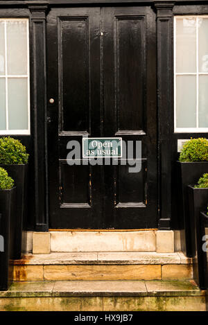 Grande vieille porte peinte noire avec mention gris Ouvrir comme d'habitude en haut de petit ensemble d'étapes de brique à Cambridge en Angleterre Banque D'Images