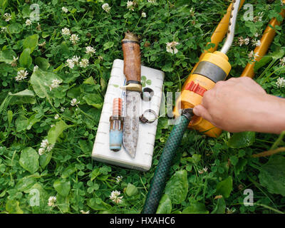 Fixation mâle un tuyau de jardin posé sur l'herbe, les outils de travail et de colliers distribués autour de Banque D'Images