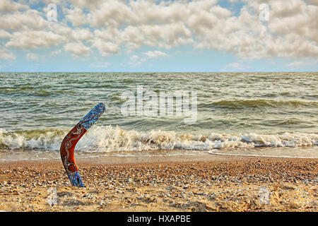 Boomerang australien multicolores sur la plage de sable contre la mer et surf de ciel dramatique.la tonalité de l'image. Banque D'Images