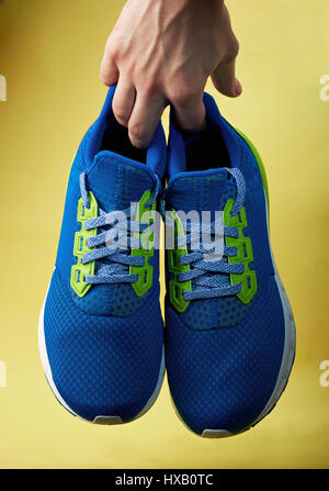 Paire de chaussures de sport bleu part maintenir isolé sur fond jaune. Holding modrn sneakers Banque D'Images