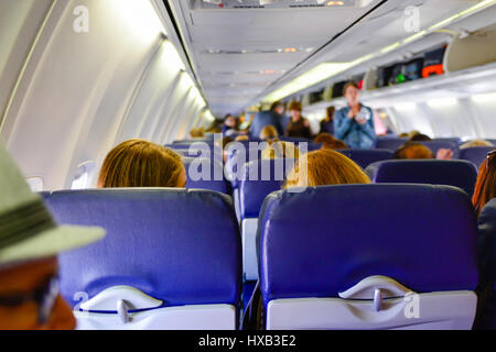 Vue de l'arrière d'un avion de ligne de la cabine avec les gens de l'embarquement, assis et en utilisant les compartiments de rangement tandis que les agents de bord rechercher sur Banque D'Images