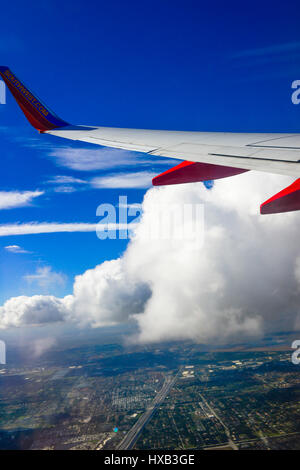 Vue aérienne de la fenêtre de l'avion de l'aile de l'avion en premier plan et nuages et ciel bleu que l'augmentation au cours d'une ville Banque D'Images