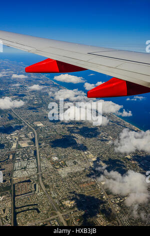 Vue aérienne de la fenêtre de l'avion de l'aile de l'avion en premier plan et nuages et ciel bleu comme avion monte sur la ville Banque D'Images