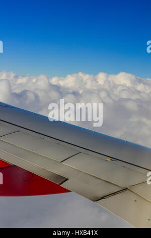 Une aile d'avion en premier plan avec des nuages blancs et ciel bleu comme vu à partir de la fenêtre de l'avion de ligne commercial Banque D'Images