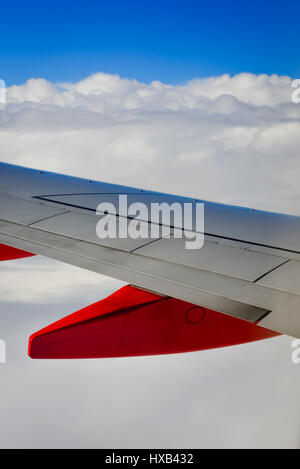 Une aile d'avion en premier plan avec des nuages blancs et ciel bleu comme vu à partir de la fenêtre de l'avion de ligne commercial Banque D'Images