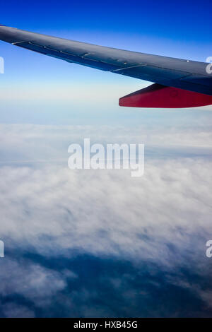 Une aile d'avion en premier plan avec des nuages blancs et ciel bleu comme vu à partir de la fenêtre de l'avion de ligne commercial Banque D'Images
