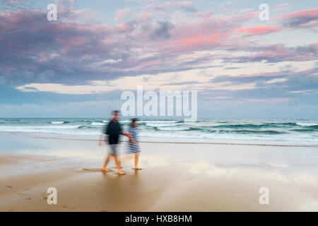 Couple en train de marcher le long des sables de plage de Bargara au coucher du soleil, Bundaberg, Queensland, Australie Banque D'Images