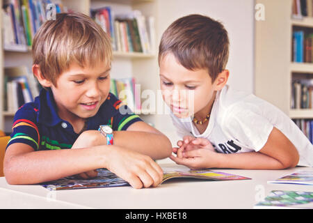 L'école les enfants assis souriant et reading book in library Banque D'Images
