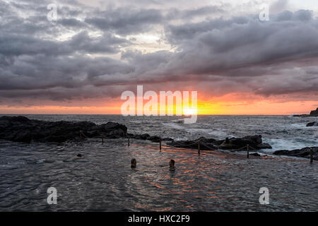 La natation de personnes devant un lever de soleil sur Kiama rock pool, Kiama, Côte d'Illawarra, New South Wales, NSW, Australie Banque D'Images