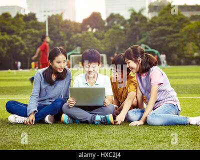 L'école élémentaire d'Asie quatre filles et garçons assis sur un ordinateur portable à l'aide de jeux ensemble. Banque D'Images