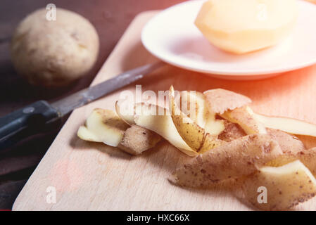 Une pomme de terre épluchée, quelques zestes et groupe des pommes de terre crues sur la table. Banque D'Images