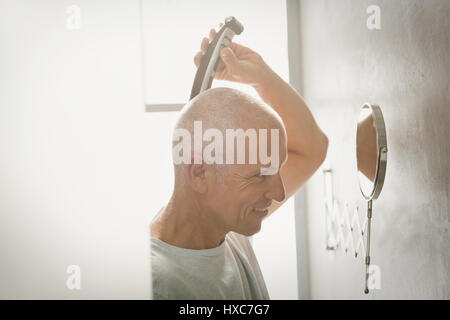 Homme mature avec tête de rasage rasoir électrique dans la salle de bains Banque D'Images