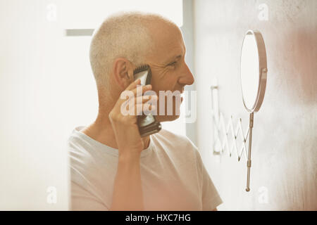 Rasage homme mûr avec agrandissement au rasoir électrique dans la salle de bains miroir Banque D'Images