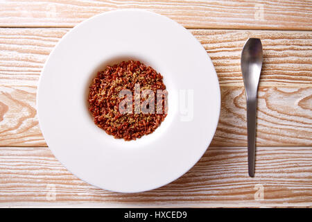 Riz sauvage rouge dans une assiette blanche sur planche de bois Banque D'Images