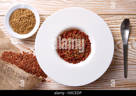 Riz sauvage rouge avec du sésame gomasio assaisonnement dans une assiette blanche sur planche de bois Banque D'Images