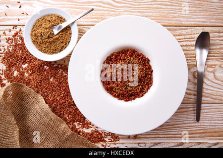 Riz sauvage rouge avec du sésame gomasio assaisonnement dans une assiette blanche sur planche de bois Banque D'Images