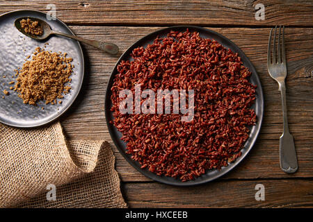 Riz sauvage rouge avec du sésame gomasio assaisonnement dans une assiette blanche sur planche de bois Banque D'Images