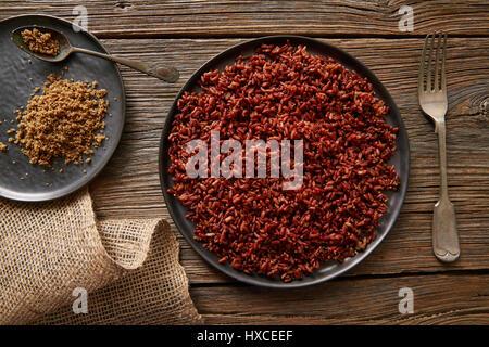 Riz sauvage rouge avec du sésame gomasio assaisonnement dans une assiette blanche sur planche de bois Banque D'Images
