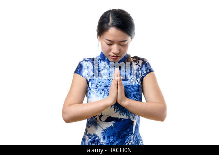 Jeune femme chinoise baissant la tête avec les mains jointes dans une salutation traditionnelle ou la prière, haut du corps isolated on white Banque D'Images