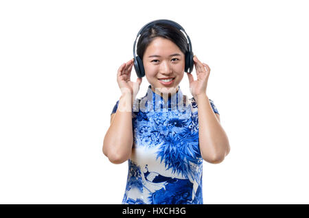 Les jeunes Chinois traditionnels Smiling woman listening to music on headphones debout souriant avec plaisir et la jouissance à l'appareil photo, isolé sur whit Banque D'Images