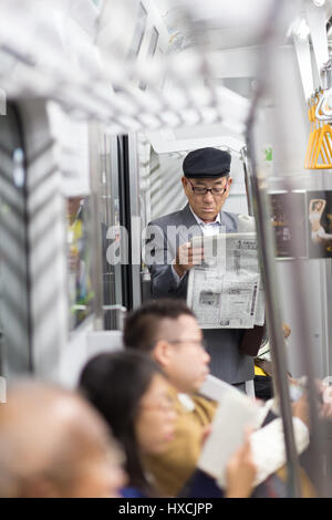 Homme d'affaires japonais prenant tour à travailler en matinée, se tenant debout à l'intérieur des transports publics et lisant le journal. Banque D'Images