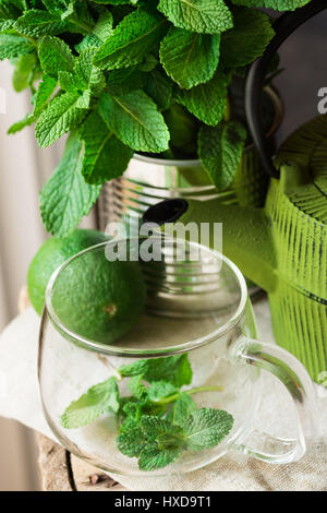 Bouquet de menthe fraîche à tin can, coupe du verre, pot, la chaux sur tissu en lin, la préparation à la préparation d'une tisane, lumière du jour, Vue du dessus Banque D'Images