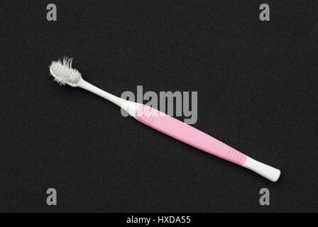 Vieille brosse à dents blanches et roses en mauvais état sur la feuille de mousse noire Banque D'Images