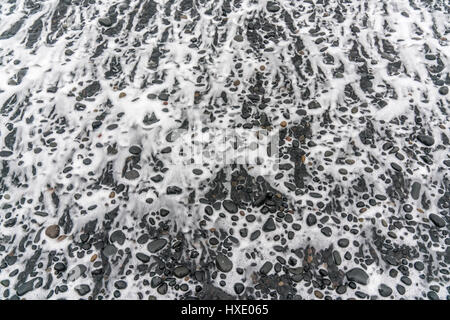 Les vagues de l'océan s'éloignent le long du surf sur une plage de sable noir en Islande Banque D'Images