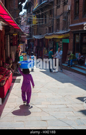 Bhaktapur, Népal - 20 mars 2015 : jeune fille portant un bassin en plastique bleu sur la tête. Banque D'Images