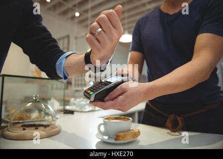 Image recadrée de payer du client avec la technologie NFC sur smart watch in coffee shop Banque D'Images