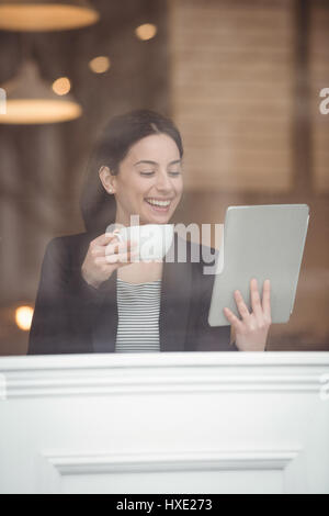 Smiling businesswoman holding digital tablet while having coffee in cafe Banque D'Images