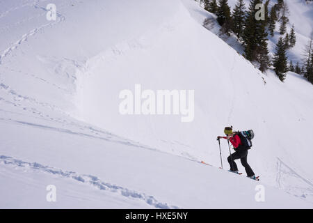 Au cours de Ski Le ski de randonnée, escalade d'une montagne enneigée sous un ciel ensoleillé, face à une corniche de neige. Banque D'Images